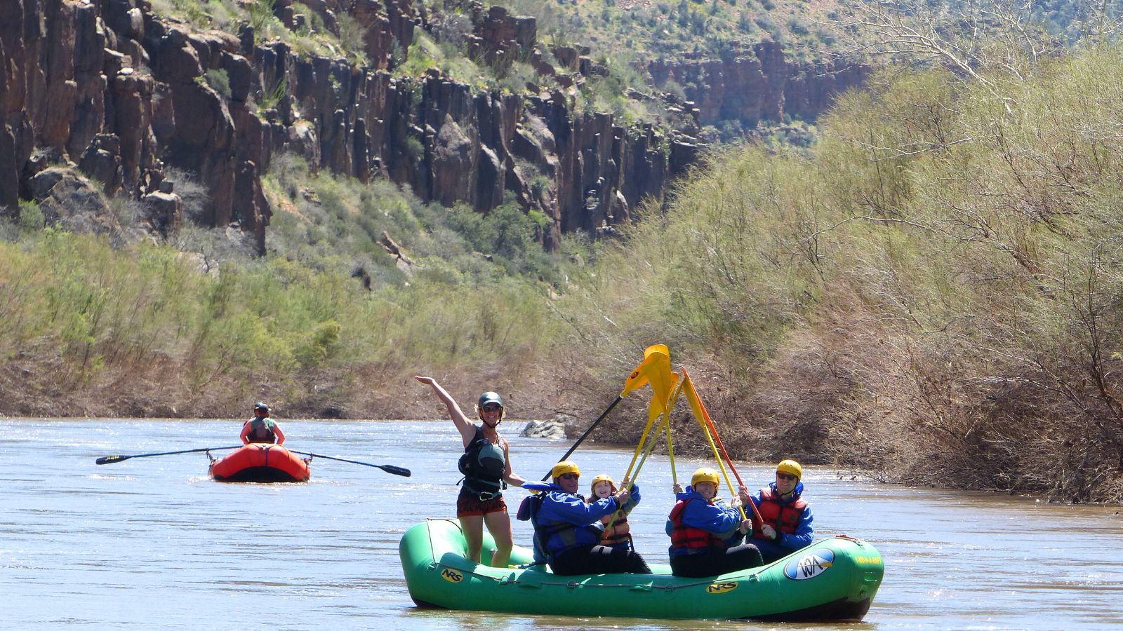 People on a river in a green boat hold their paddles up