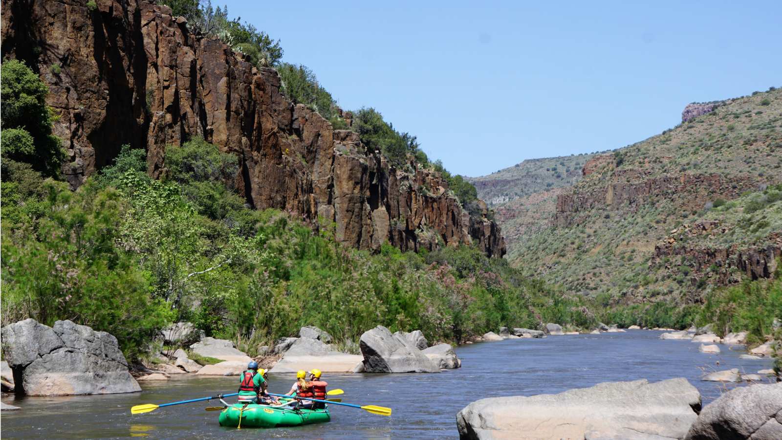 a green raft floats down a desert canyon