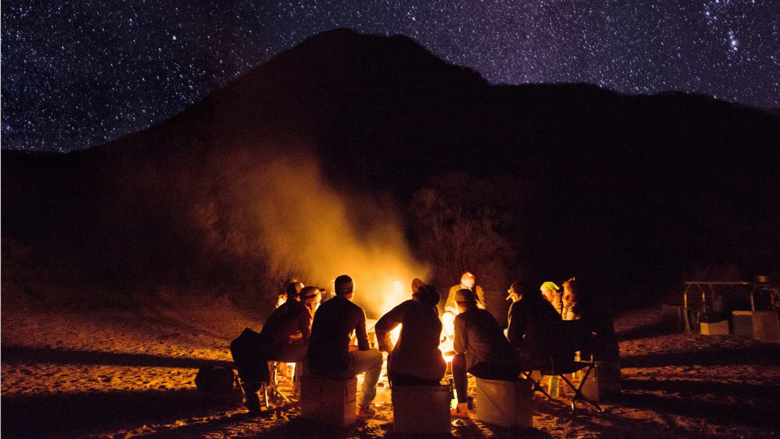 a group of people sit around a fire at night