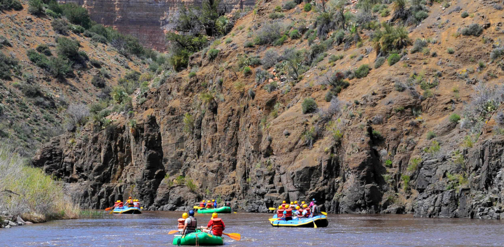 Green boats float down the salt river against a scenic rock face