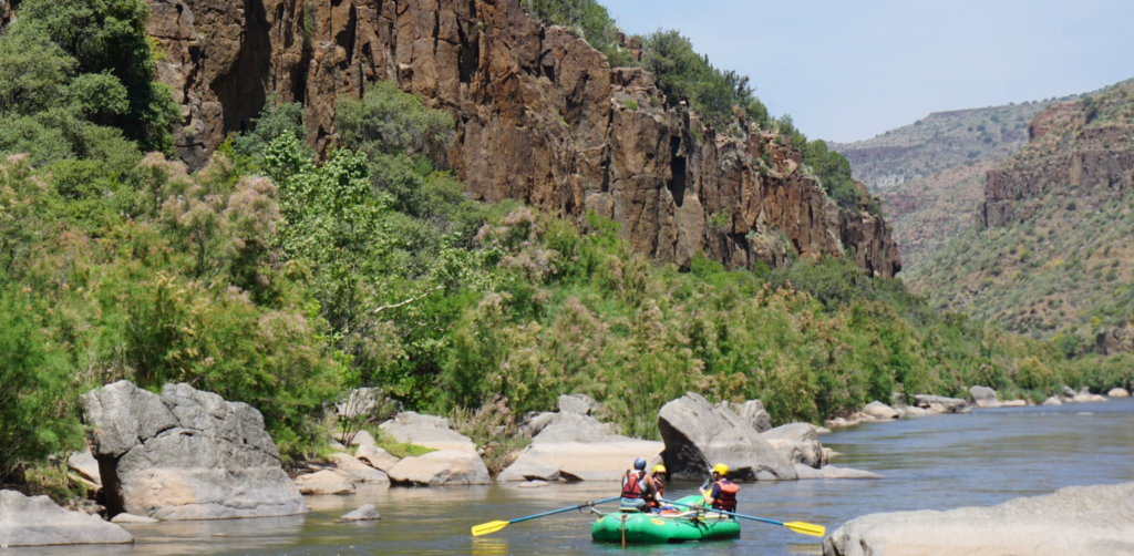 A green raft with yellow paddles floats down the salt river with interesting rock formations