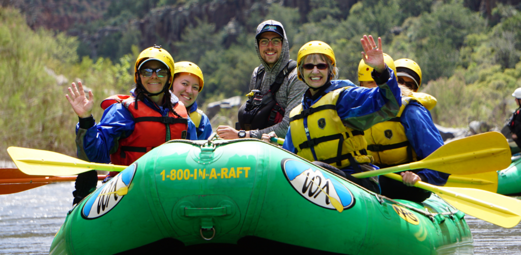 People in yellow helmets in a raft on the salt river smile and wave