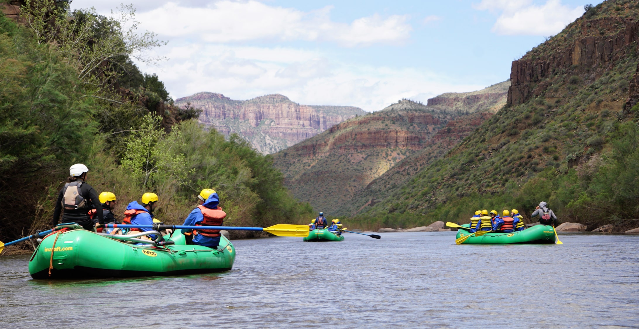 three green boats float down a river