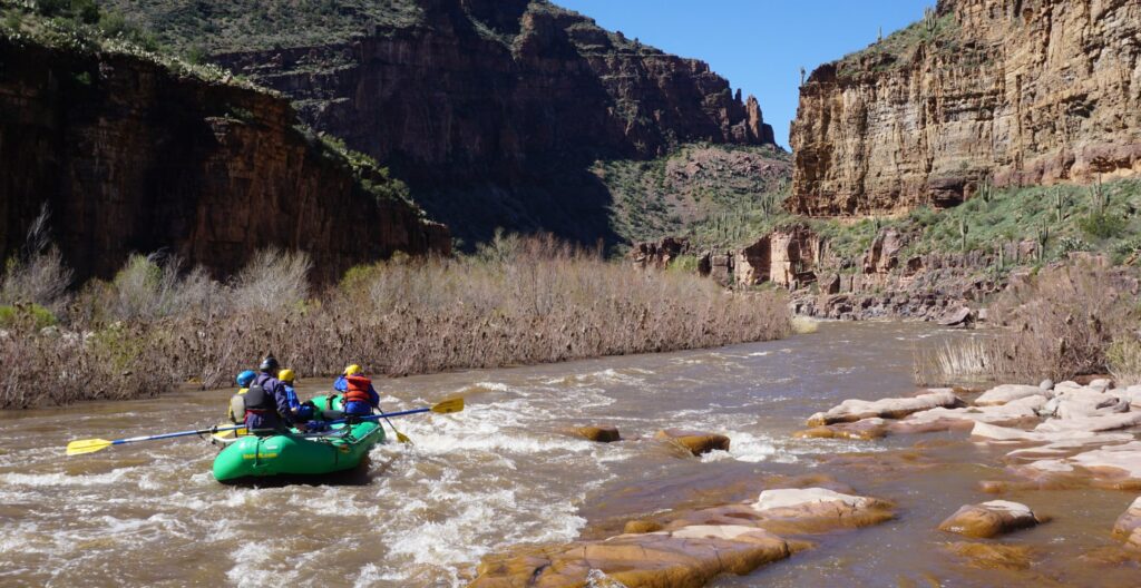 rafters in a green boat raft through a canyon