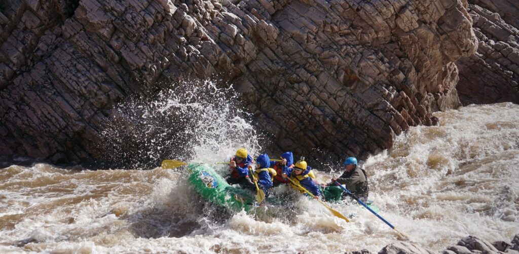 rafters in a green boat navigate white water