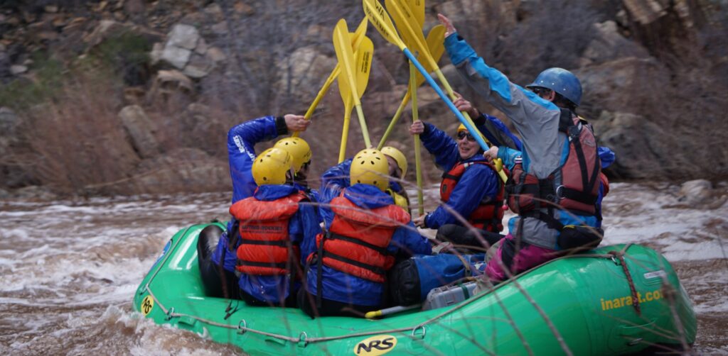 Rafters in a green boat hold up yellow paddles