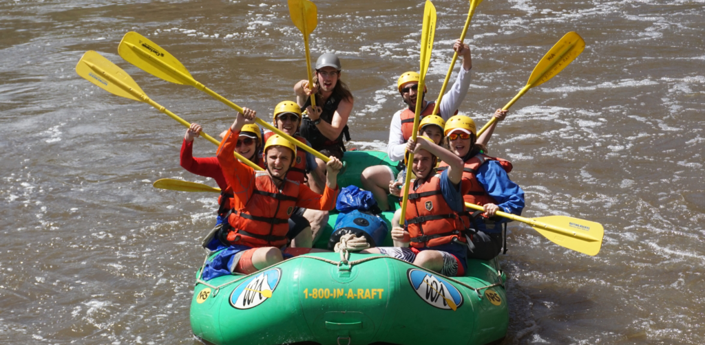 People on a green raft with yellow paddles and helmets celebrate after a white water rapid