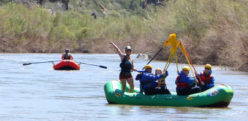 A family on a boat on the salt river raise their paddles and smile