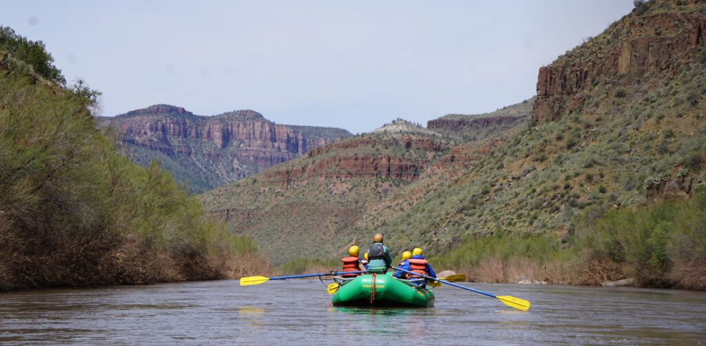 A green raft paddles away in the desert