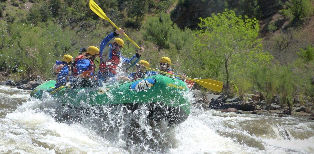 A green boat full of people plunges through whitewater