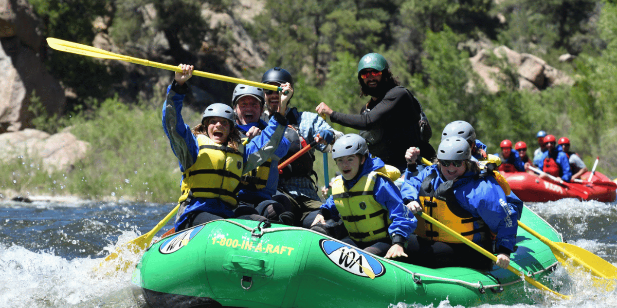 Rafting group in a river rapid lifting their paddles up.